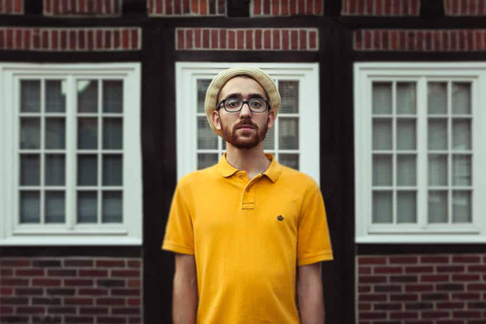 A color photo of a male model in yellow t-shirt posing outdoors
